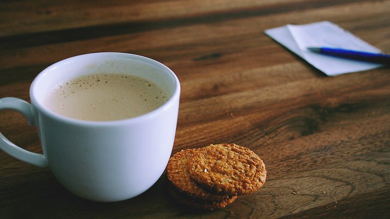 Transitional care- photo of a white coffee cup, two biscuits, pen and paper on a wooden table