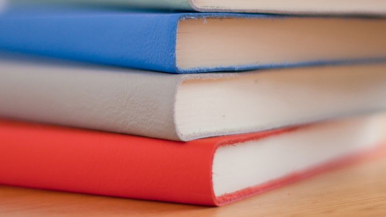 Cropped photo of a pile of four note books. One with a red cover, one blue and one grey