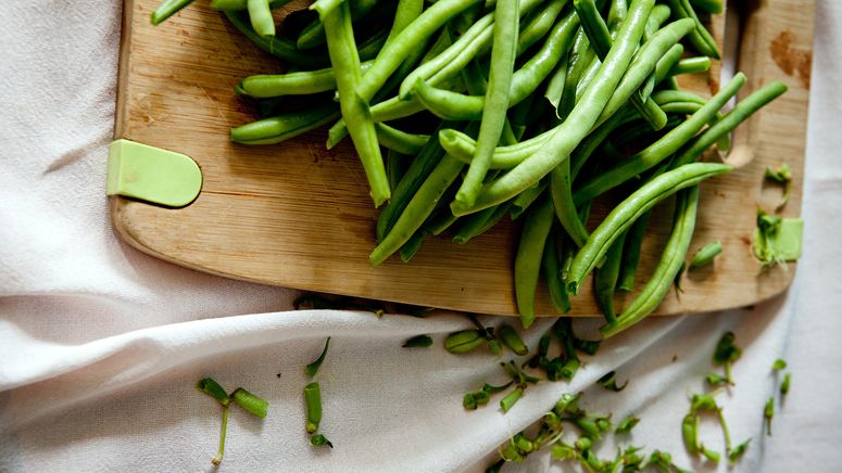 Home care package providers- cropped photo of green beans on a wooden chopping board and white cloth underneath