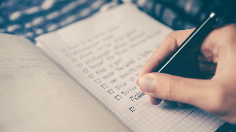 Photo of a hand holding a pen writing a post operative checklist in a small notebook