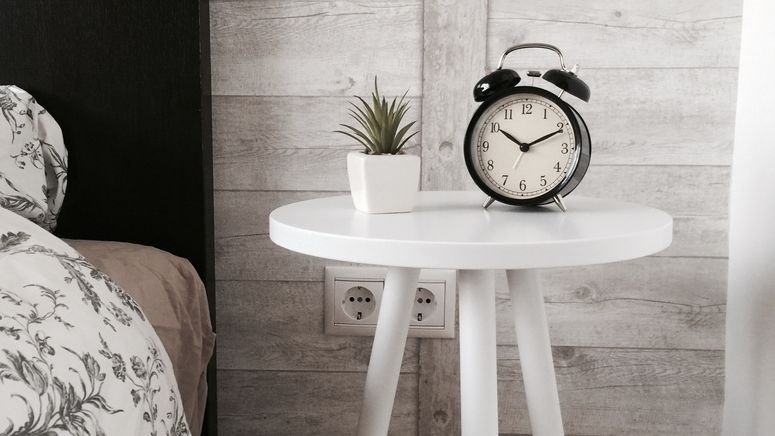 Advanced care planning- Cropped photo of a round white bedside table with an alarm clock and succulent pot next to a bed