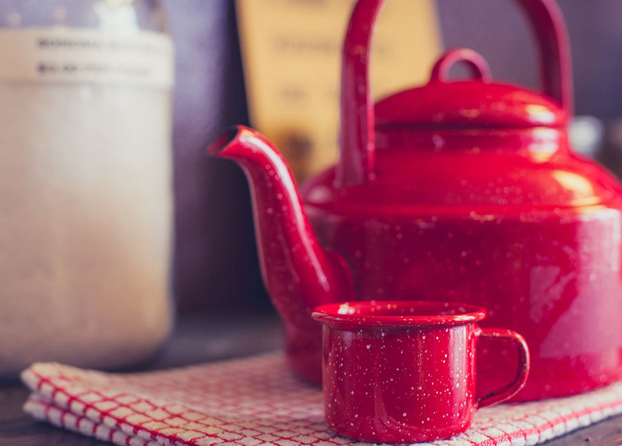 Spending your home care package- photo of a red kettle and mug sitting on a red and white checked tea towel on a shelf with sugar in the background