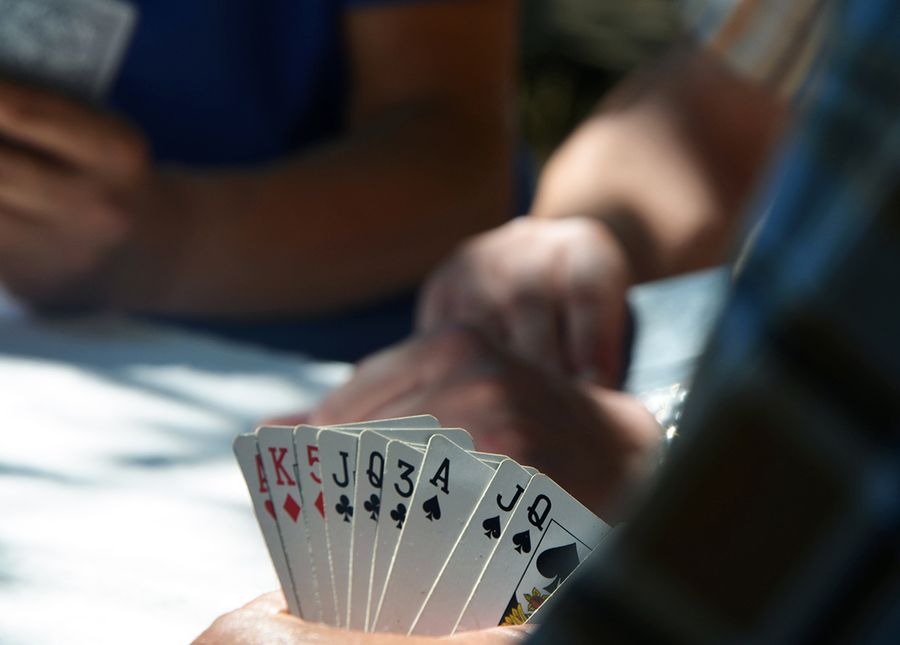 Aged care quality standards- Cropped photo of three pairs of hands playing cards, the pair in the foreground are holding a mixed hand