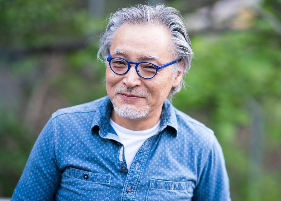 Transitional care- photo of an asian man with grey hair smiling at the camera in a blue shirt and blue round glasses
