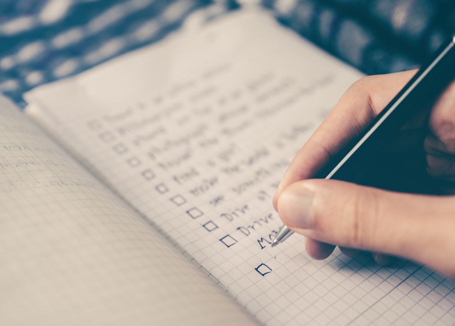 Photo of a hand holding a pen writing a post operative checklist in a small notebook