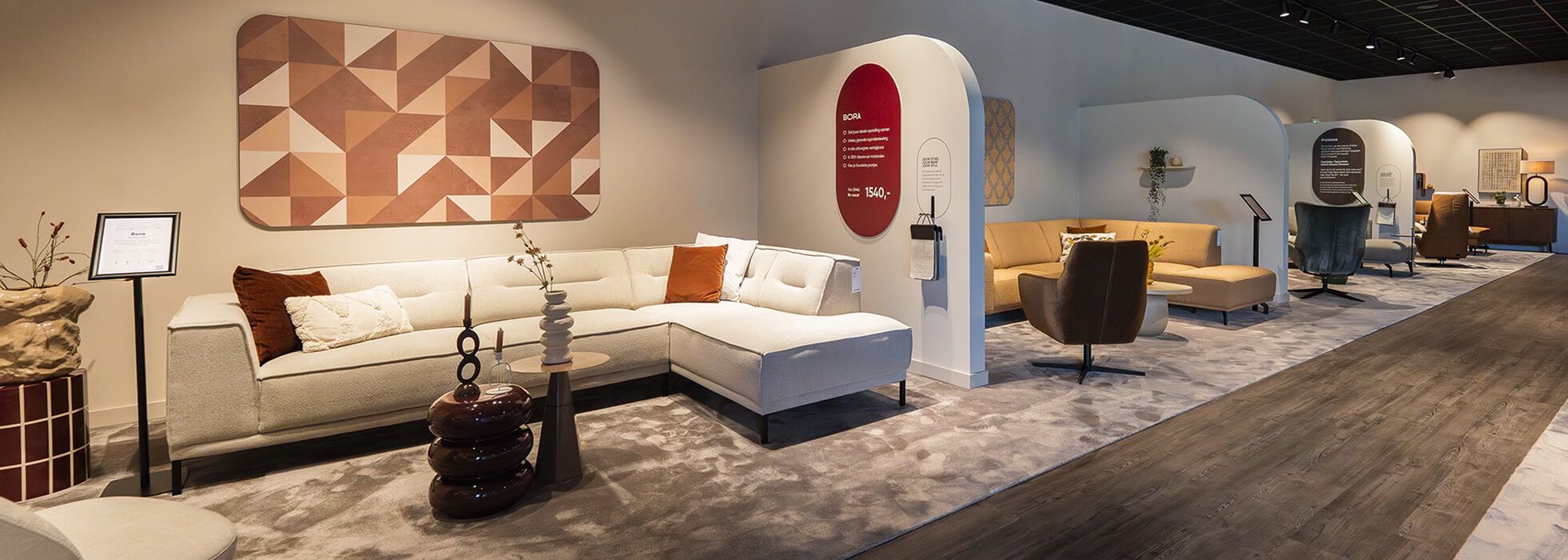 Modern furniture showroom featuring stylish sectionals, armchairs, decorative tables, and geometric wall art on a wooden floor.