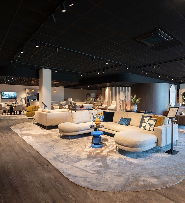 A modern furniture showroom with stylish sofas, colorful cushions, and decorative items on display, illuminated by overhead lighting.