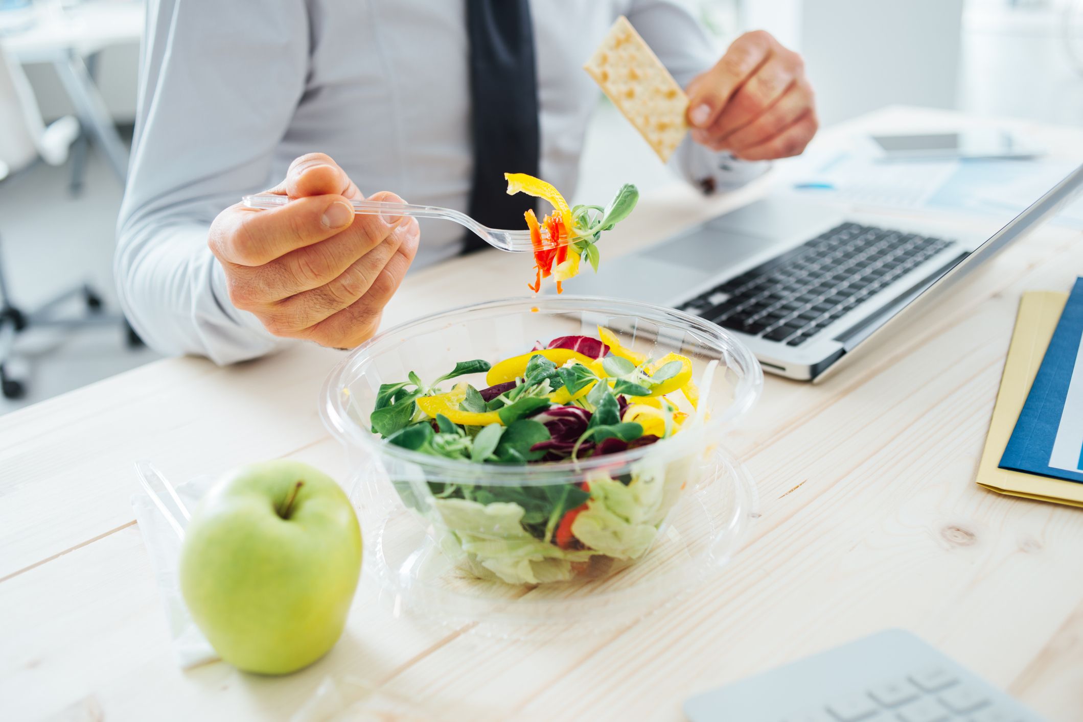 Employee eating lunch at desk with computer and boxed meal