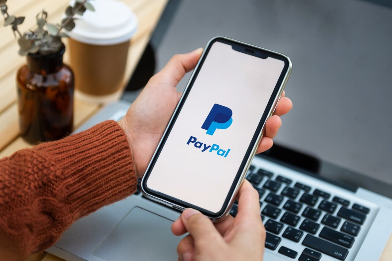 PayPal pro začátečníky - Žena drží nad notebookem telefon v ruce s nápisem PayPal