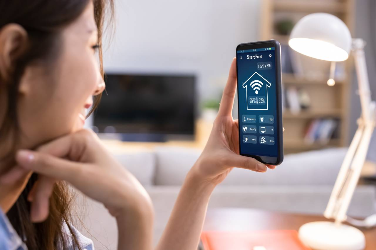 Internet věcí - Žena drží mobil a ovládá chytrou domácnost