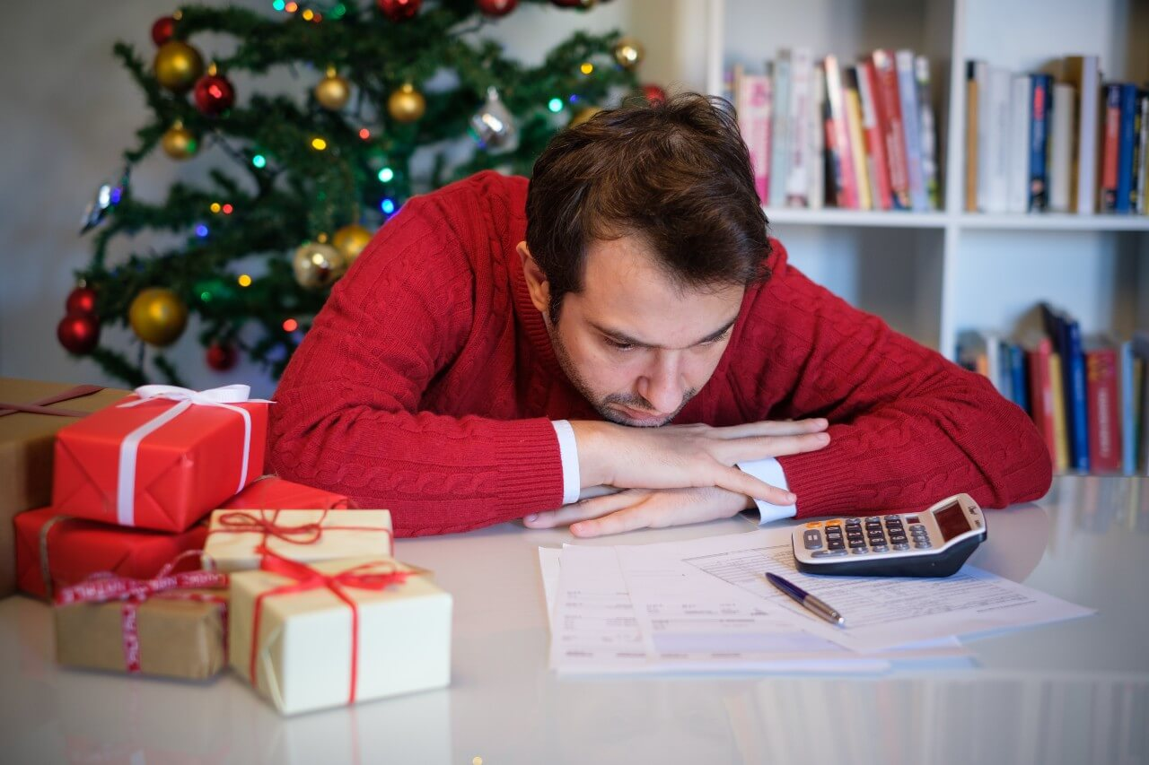 Půjčka na bydlení a dárky - muž v červeném svetru, dárky, kalkulačka, papíry a propiska na stole