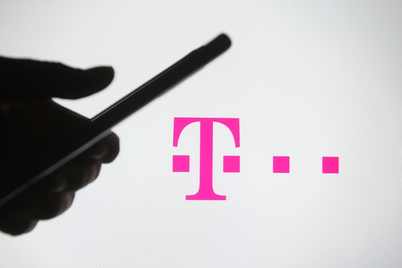 Ruka s mobilním telefonem v ruce, v pozadí logo T-Mobile