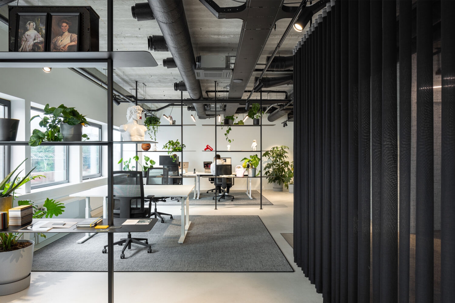Lichte kantoorruimte met planten, open werkplekken, kunstobjecten en zwarte roomdividers