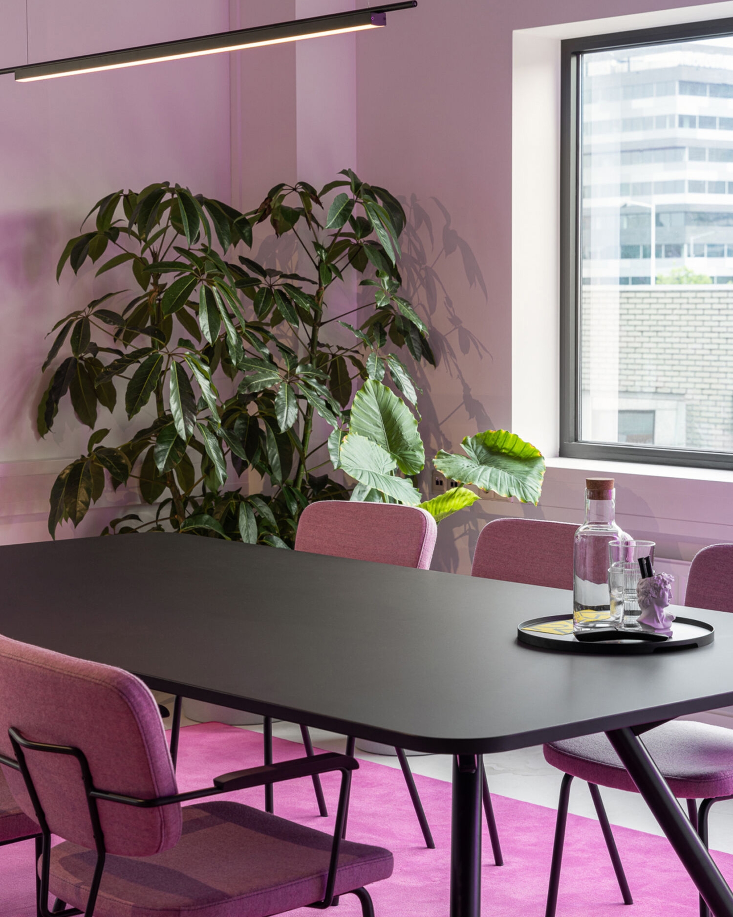 Vergaderruimte met zwarte tafel, roze stoelen, grote planten en paarse sfeerverlichting