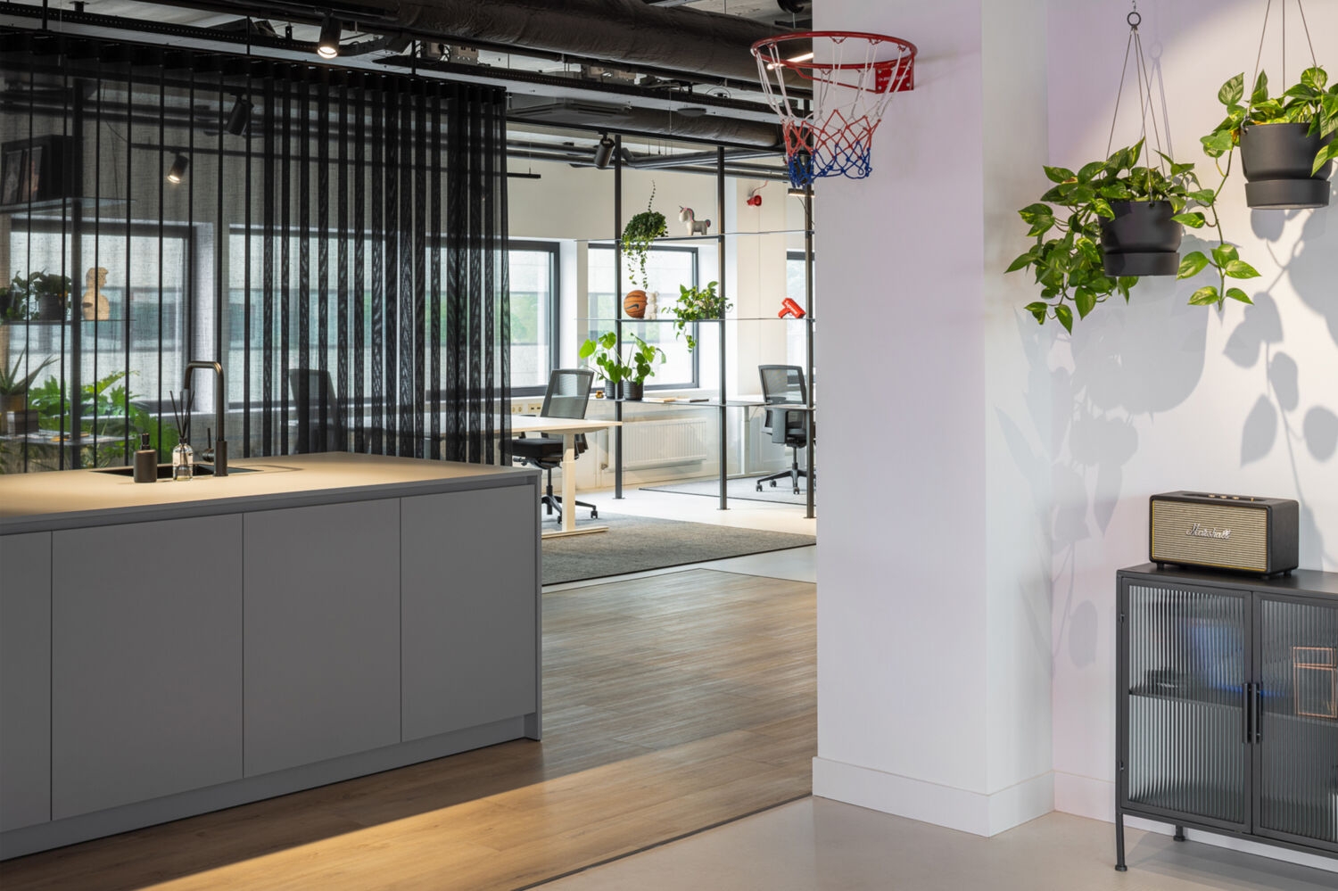 Kantoorinterieur met werkplekken, hangplanten, een basketbalring en zwarte roomdividers