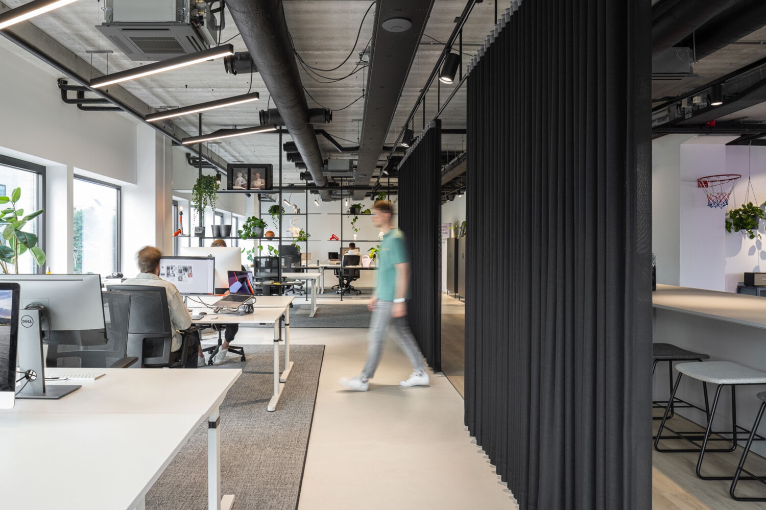 Open office space with workstations, black curtains, and an employee walking through the space