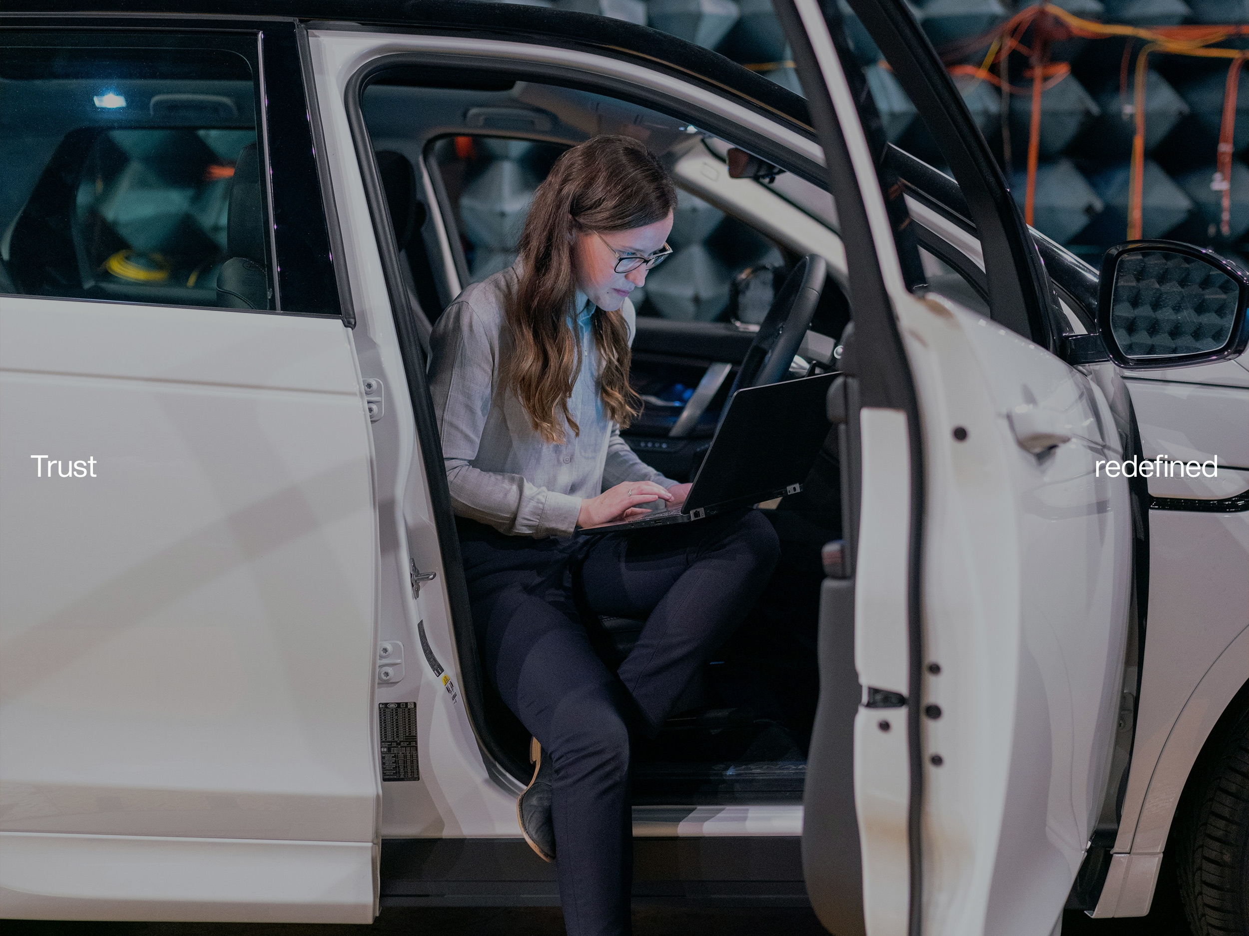 Vrouw werkt op een laptop vanuit een open auto met de tekst ‘Trust redefined’