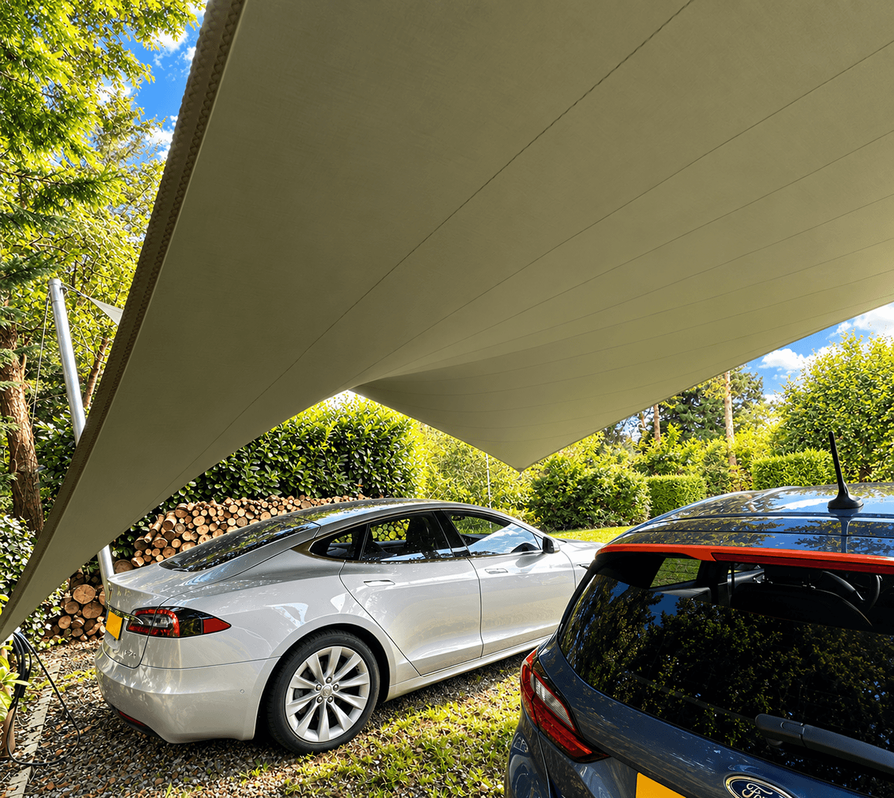 Twee auto’s geparkeerd onder een groene design carport van gespannen textiel in een bosrijke tuin.