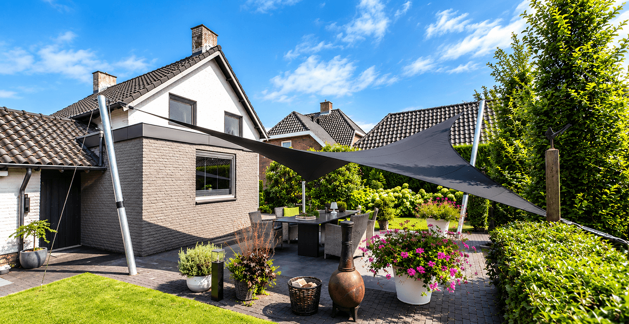 Maatwerk membraanoverkapping boven een terras aan huis met eettafel en omliggende tuin.