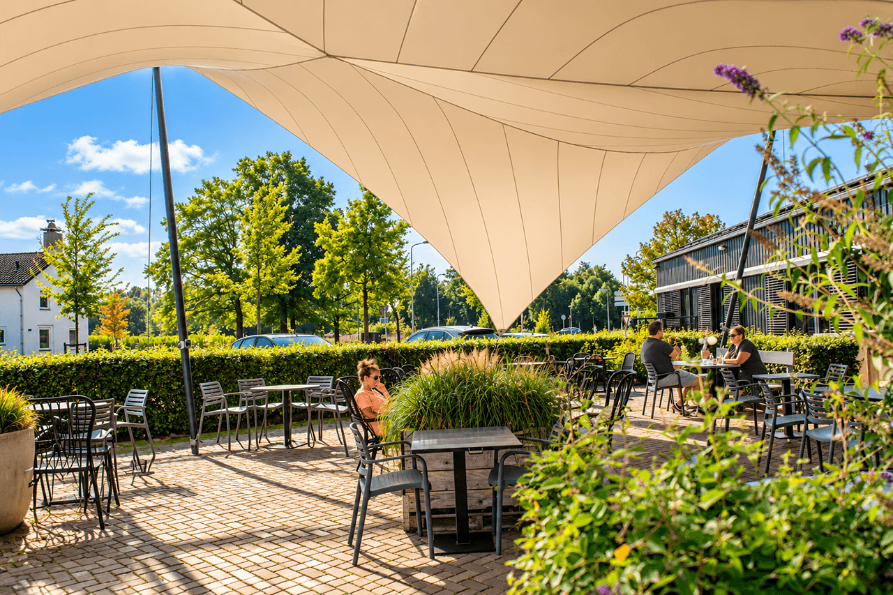 Maatwerk design schaduwdoek boven een ruim horecaterras met zitplaatsen.