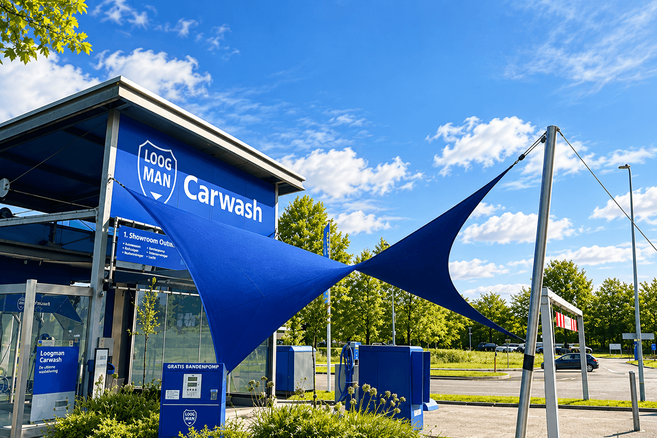 Blauw maatwerk schaduwdoek bij een carwash, gespannen tussen het gebouw en vrijstaande masten.