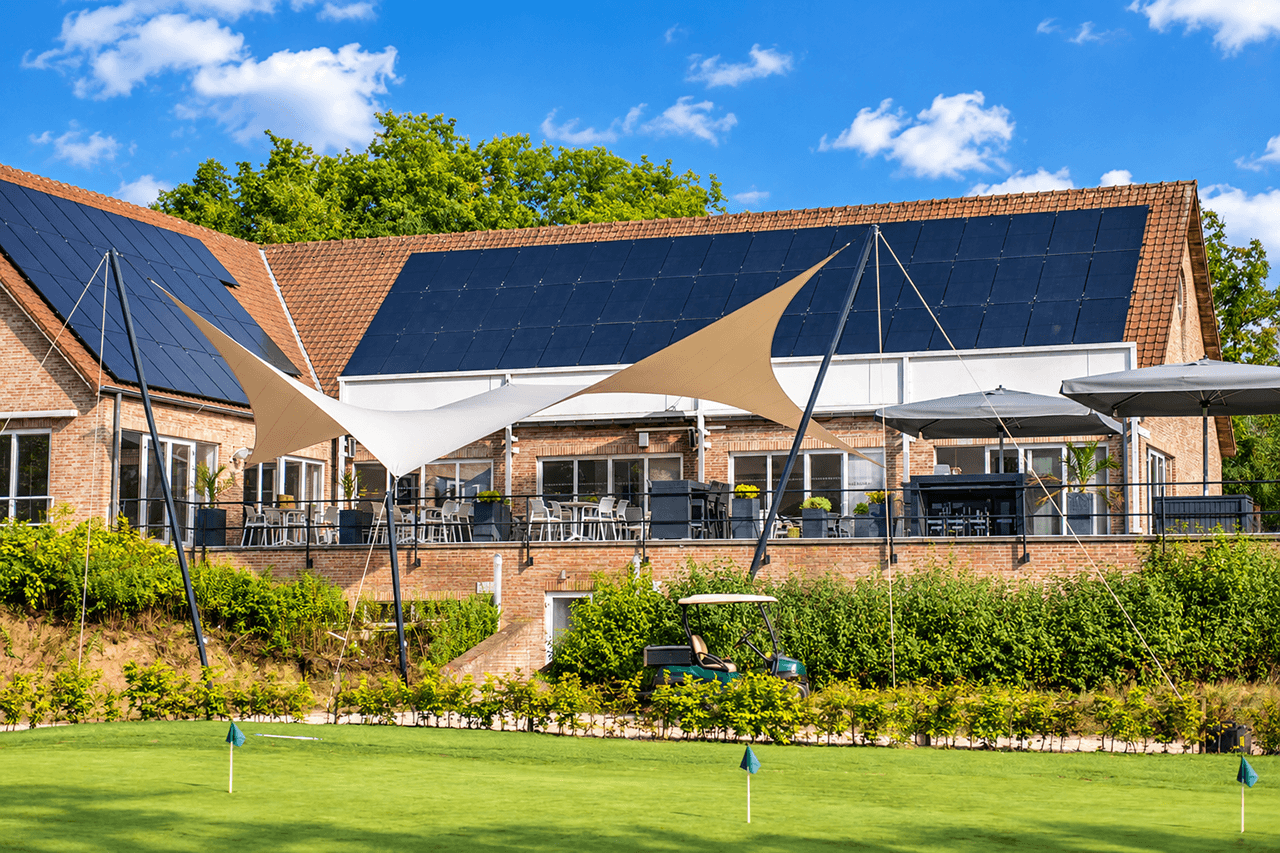 Twee maatwerk zonnedoeken boven het terras van een golfclub, gespannen tussen hoge masten.