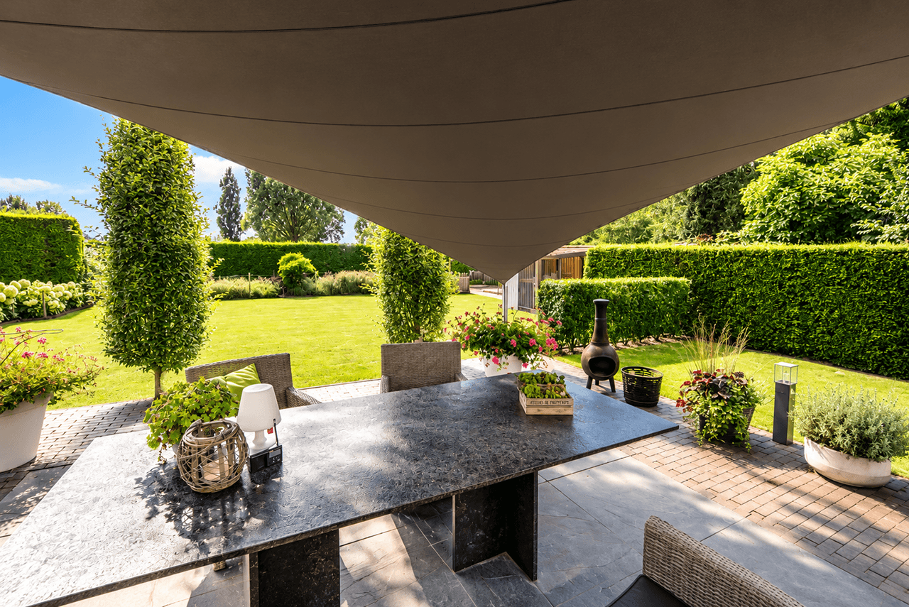 Maatwerk membraanoverkapping boven een terras met eettafel en uitzicht op een ruime tuin.