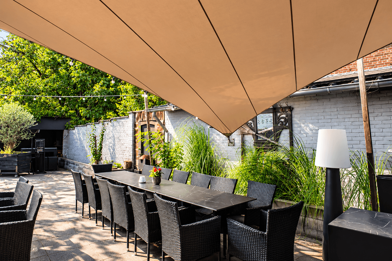Maatwerk membraanoverkapping boven een terras met een lange eettafel en zitplaatsen.