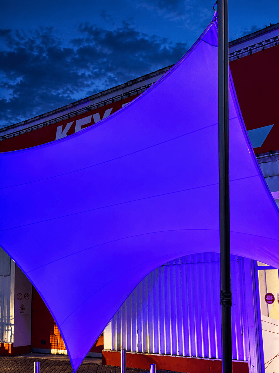 Verlichte textiele overkapping van Mobuline bij een bedrijfslocatie, sfeervol uitgelicht in de avond.