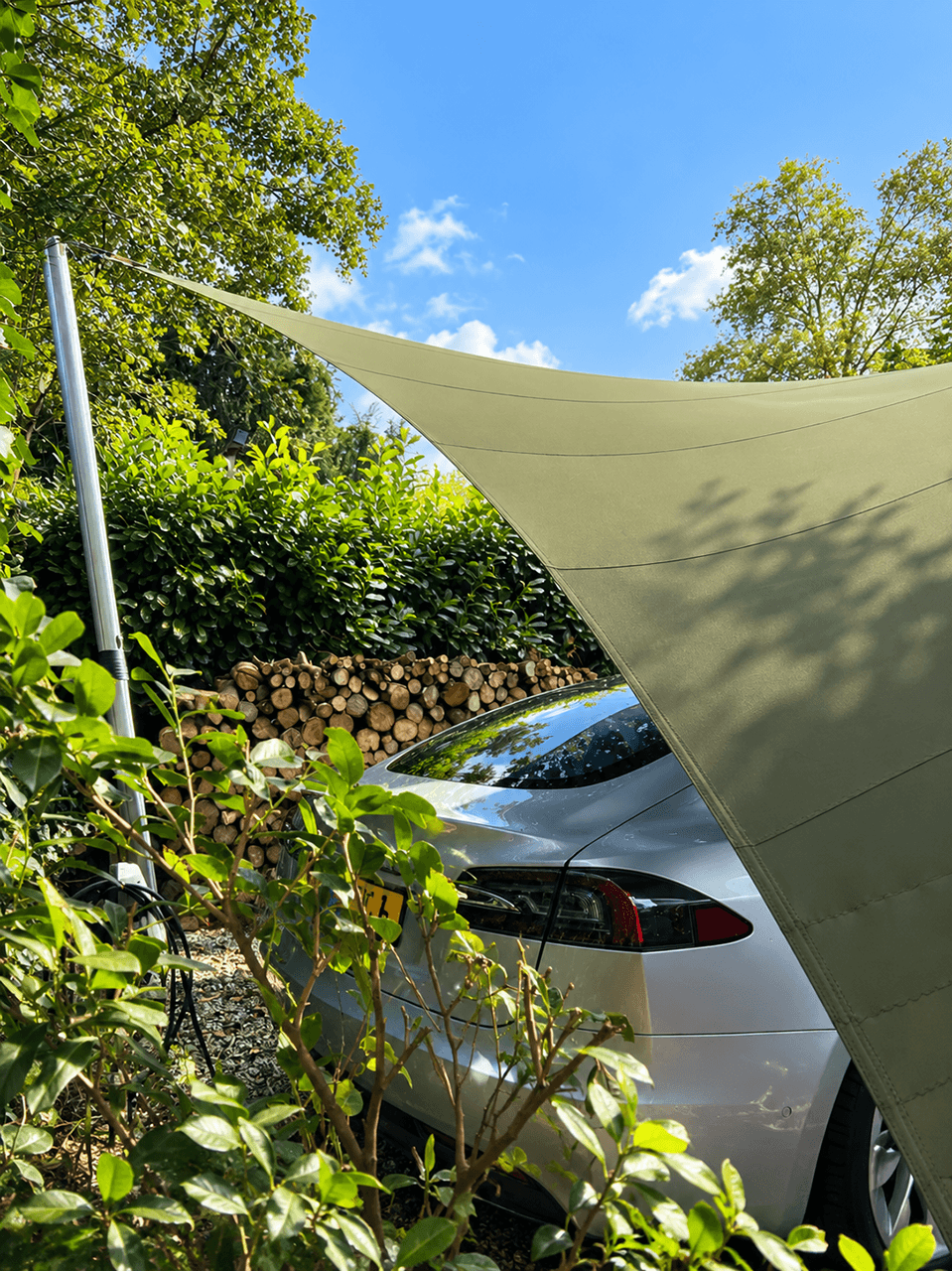 Detail van een textiele design carport boven een geparkeerde auto, omringd door beplanting.