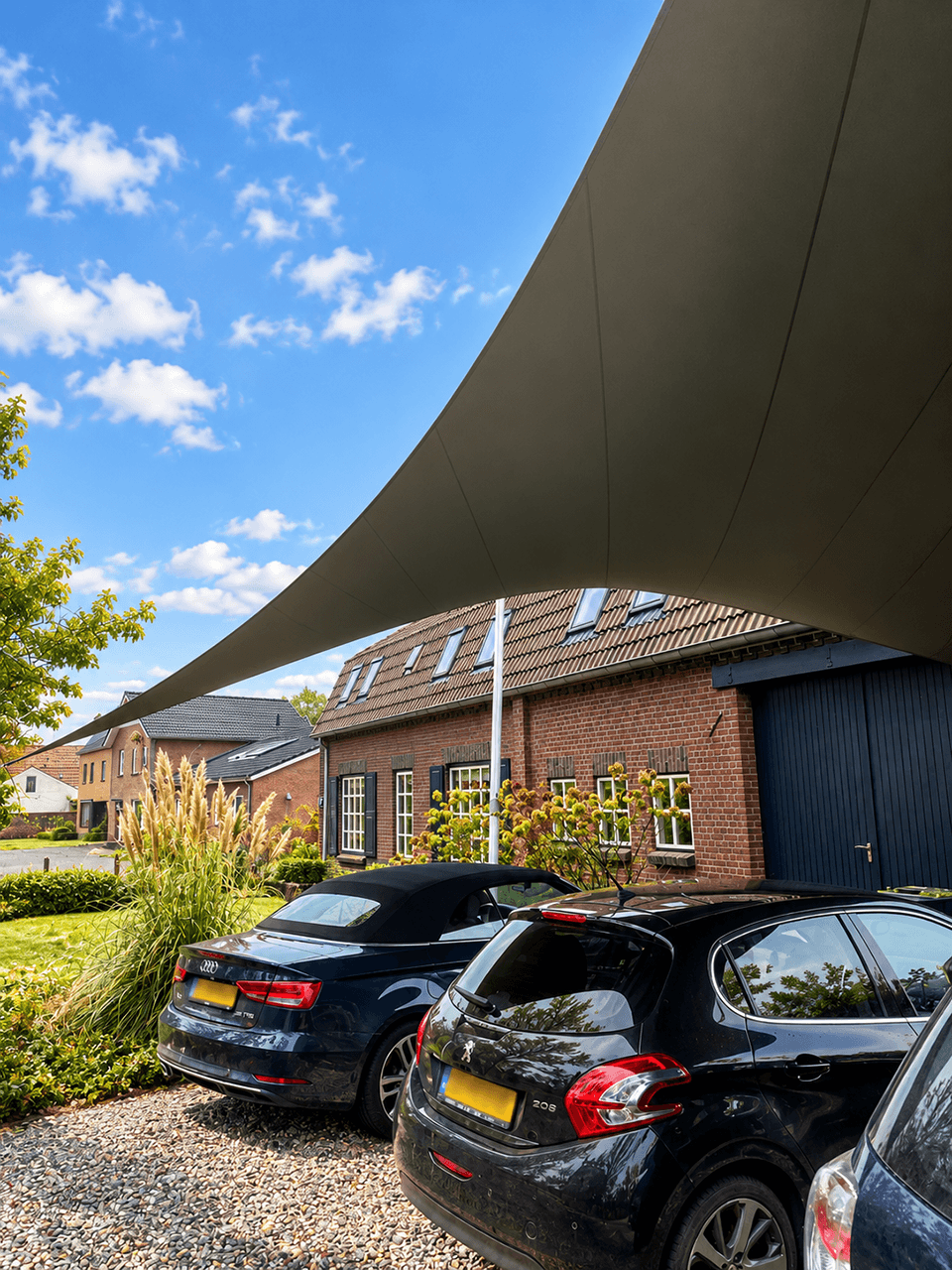 Groot maatwerk schaduwdoek als overkapping boven meerdere parkeerplaatsen bij een woning.