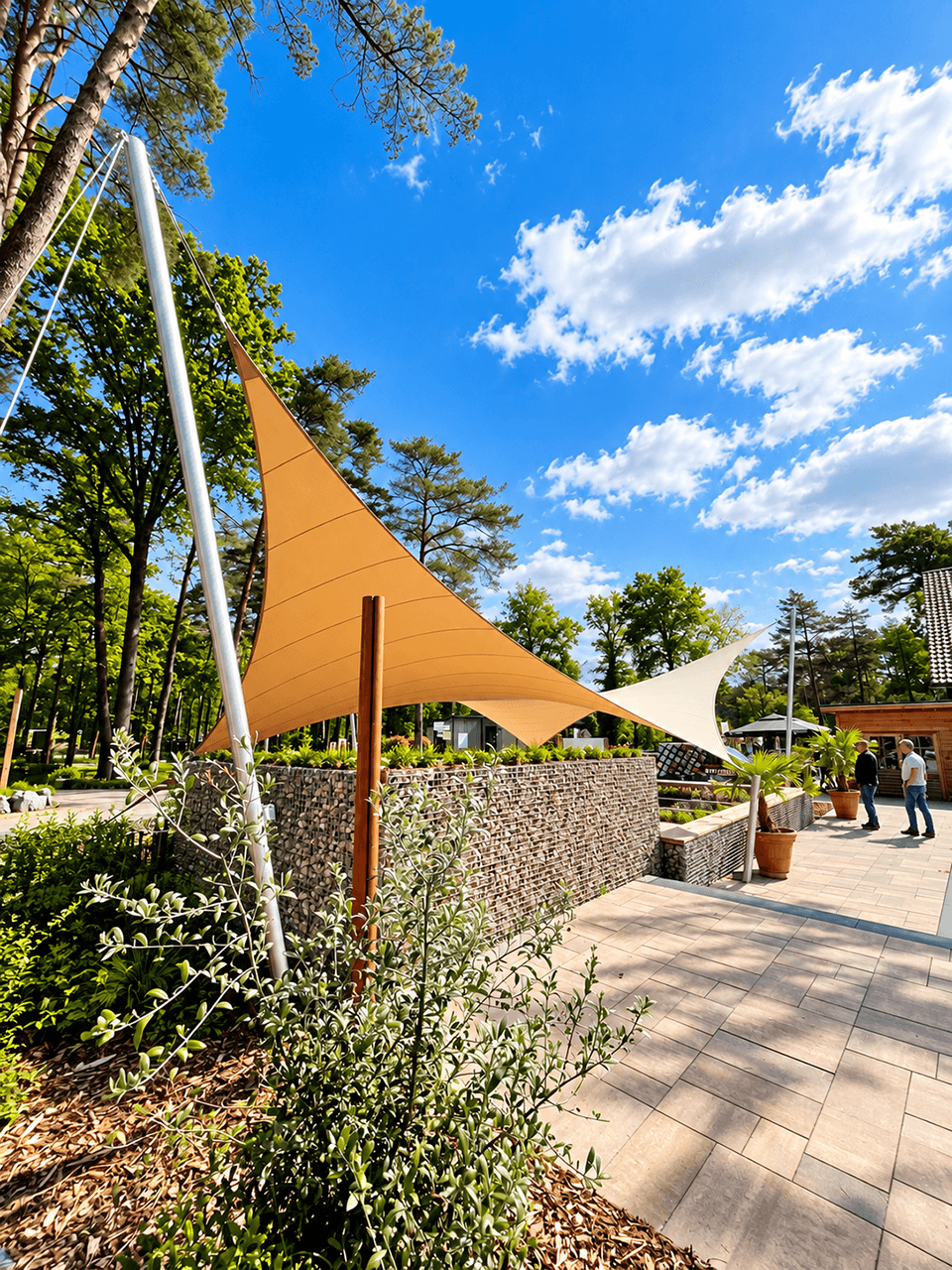 Maatwerk zonnedoeken gespannen tussen hoge masten boven een terras op een vakantiepark.
