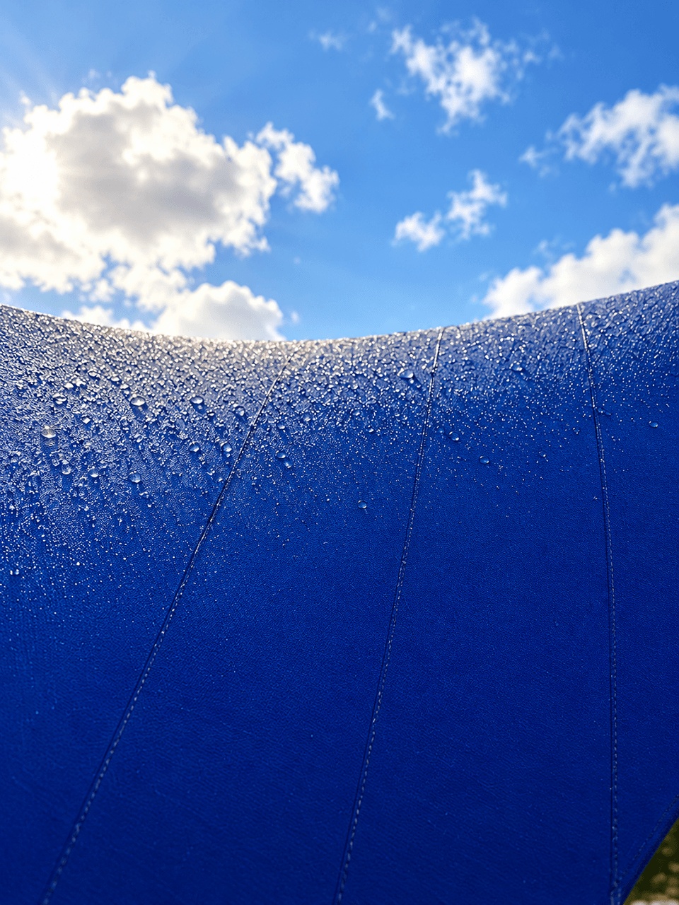 Close-up van een blauw gespannen schaduwdoek met regendruppels op het textiel.