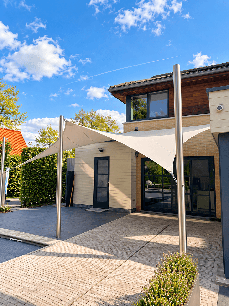 Twee textiele overkappingen bij een moderne woning, gespannen tussen vrijstaande masten en de gevel.