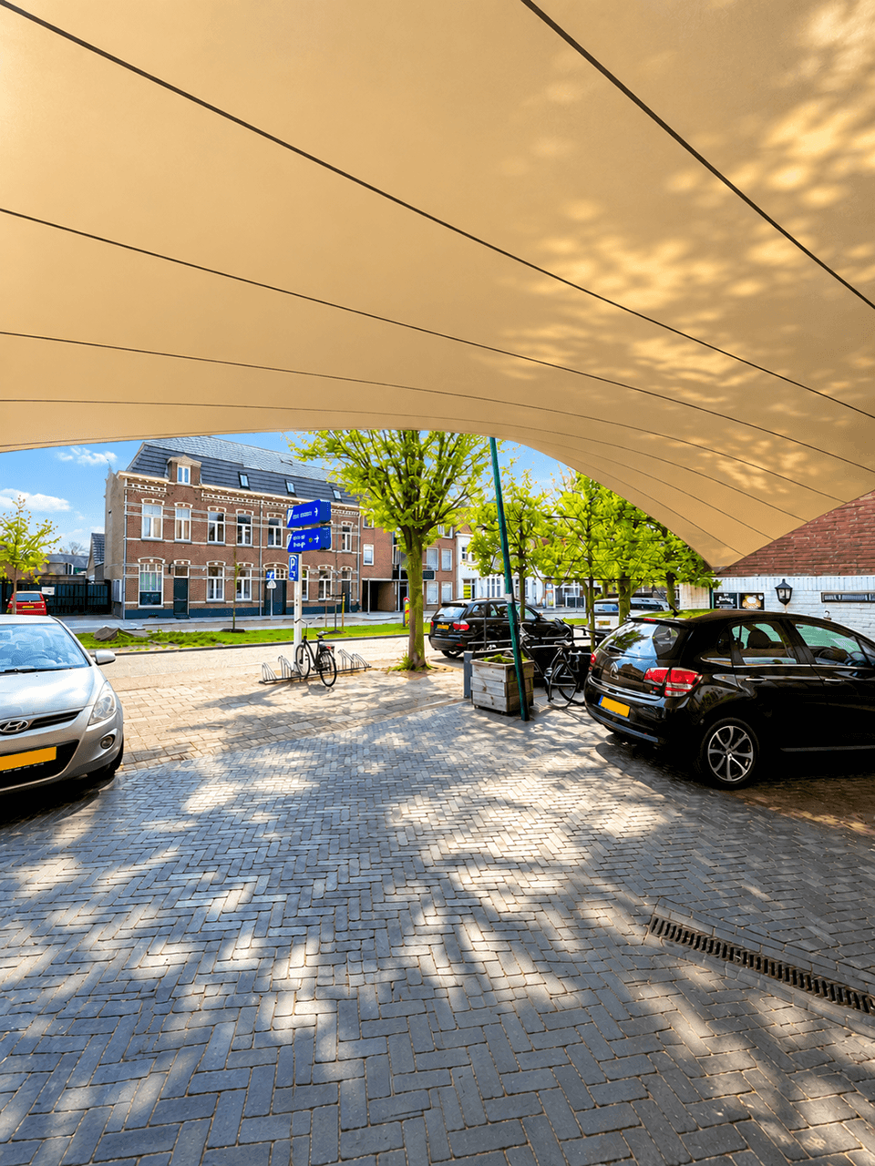 Maatwerk textiele overkapping boven een parkeer- en buitenruimte bij een stedelijk pand.