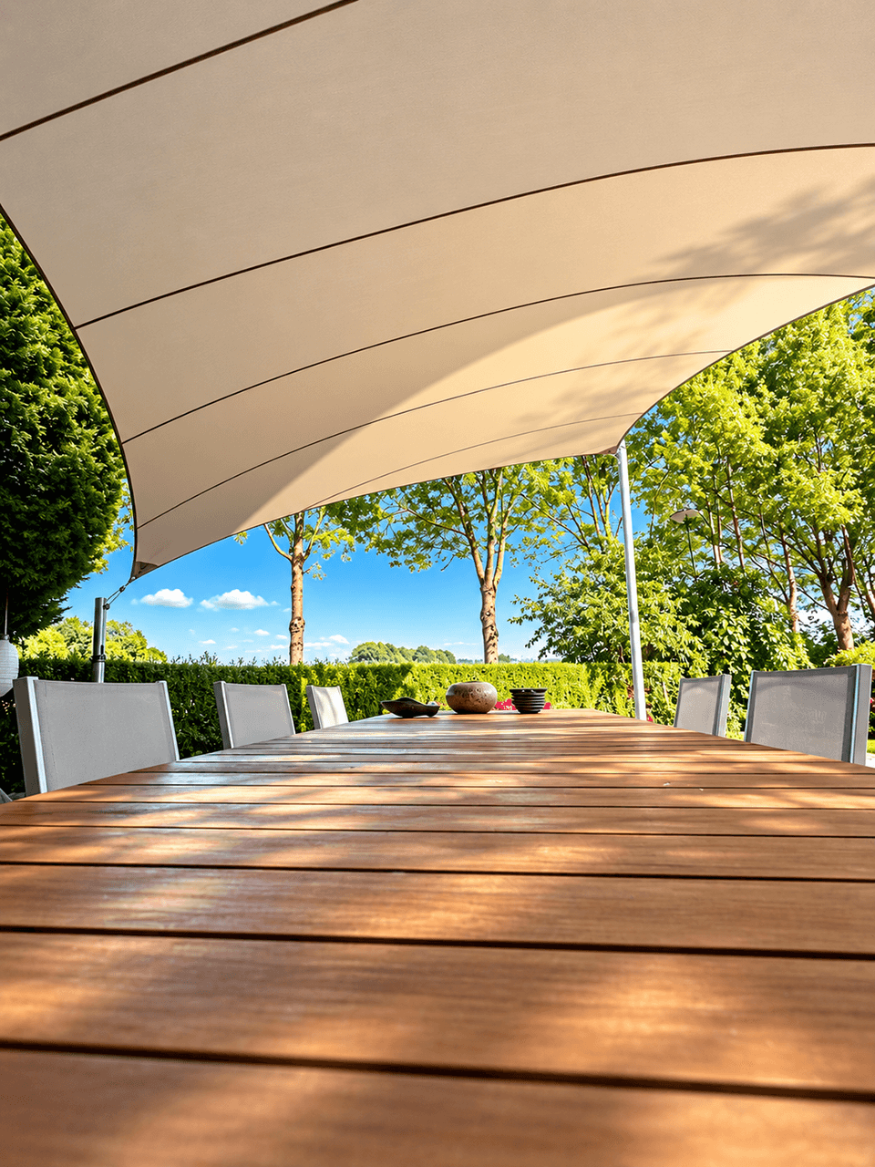Luxe design schaduwdoek boven een ruim terras met eettafel, omringd door een groene tuin.