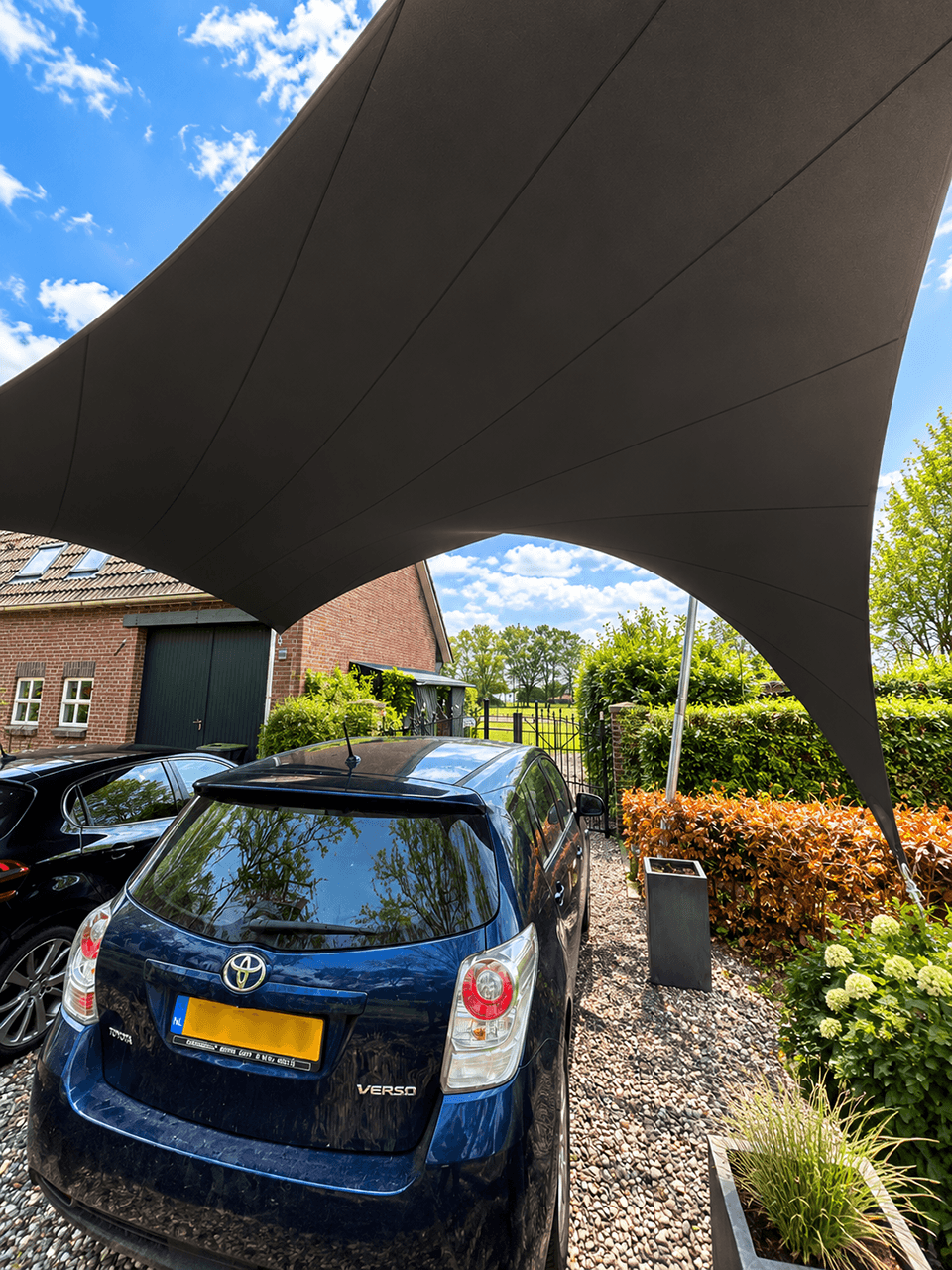 Textiele design carport boven meerdere geparkeerde auto’s bij een woning.