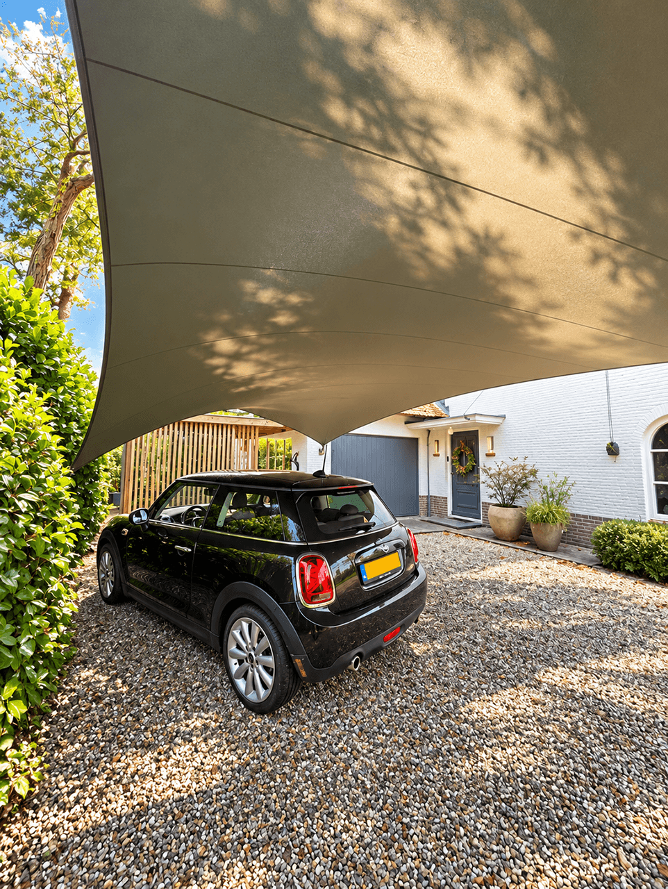 Maatwerk schaduwdoek als carport boven een zwarte auto bij een woning.