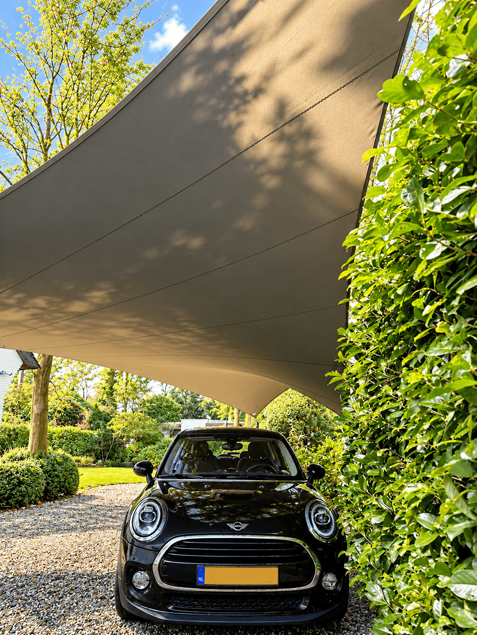 Donker maatwerk schaduwdoek als carport boven een auto, passend in een groene tuin.