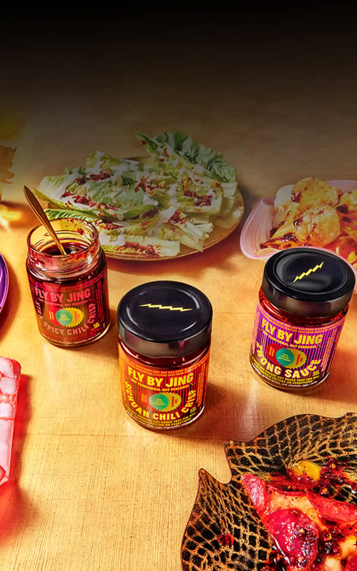 Four jars of Fly By Jing products on a table spread of dishes
