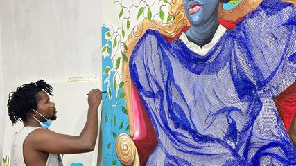 Adjei Tawaiah adding blue paint to a large, mixed media canvas