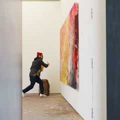 José Parlá striding towards a large abstract painting, paintbrush in hand