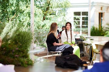 Gemma Rolls Bentley interviewing Gisela McDaniel in a leafy outdoor space