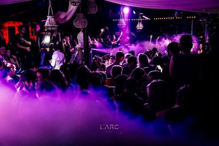 A lively scene at L'Arc Paris nightclub, showcasing a vibrant crowd basking in colorful lights and swirling fog, capturing the essence of an exciting night out.