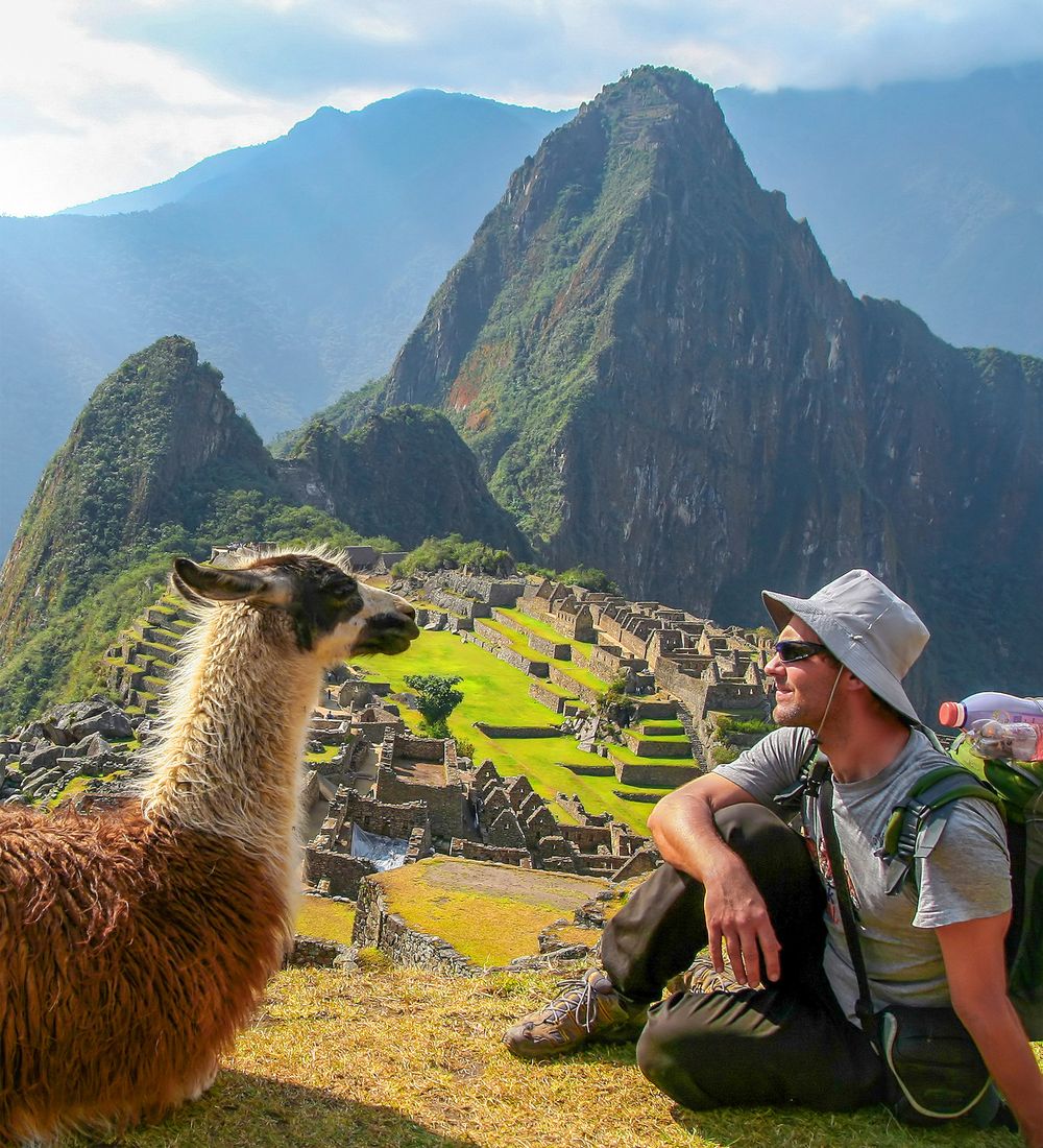 tourist and llama sitting in front of machu picchu peru