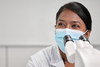 Bild zeigt Roche-Mitarbeiterin mit Mundschutz vor dem Mikroskop