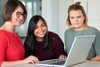 Bild zeigt drei Frauen, die lächeln und auf einen Laptop-Bildschirm schauen.