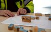 Male wearing hi-vis pointing at paper with wooden blocks in the foreground