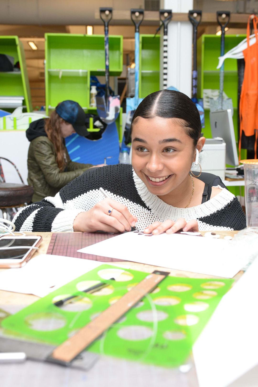 A girl looking up and smiling while cutting paper with a x-acto knife