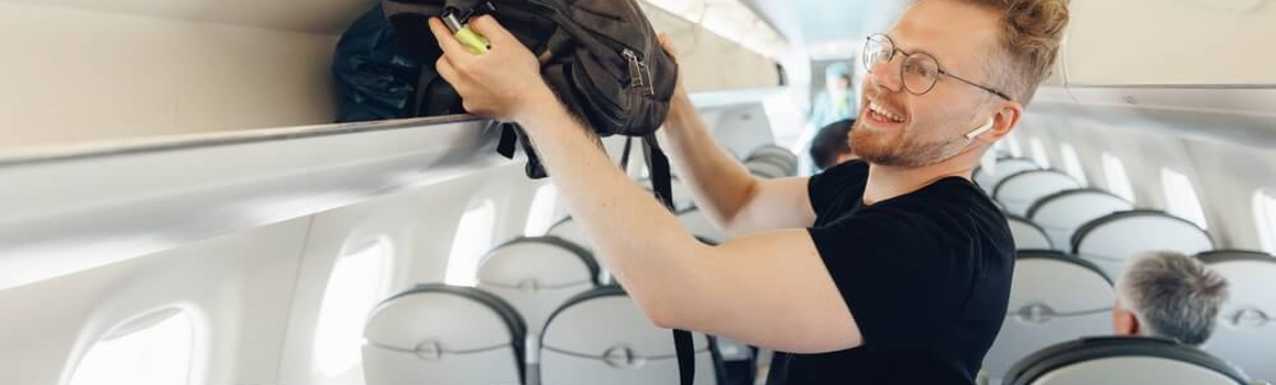 Muž v letadle ukládá batoh do zavazadlového prostoru